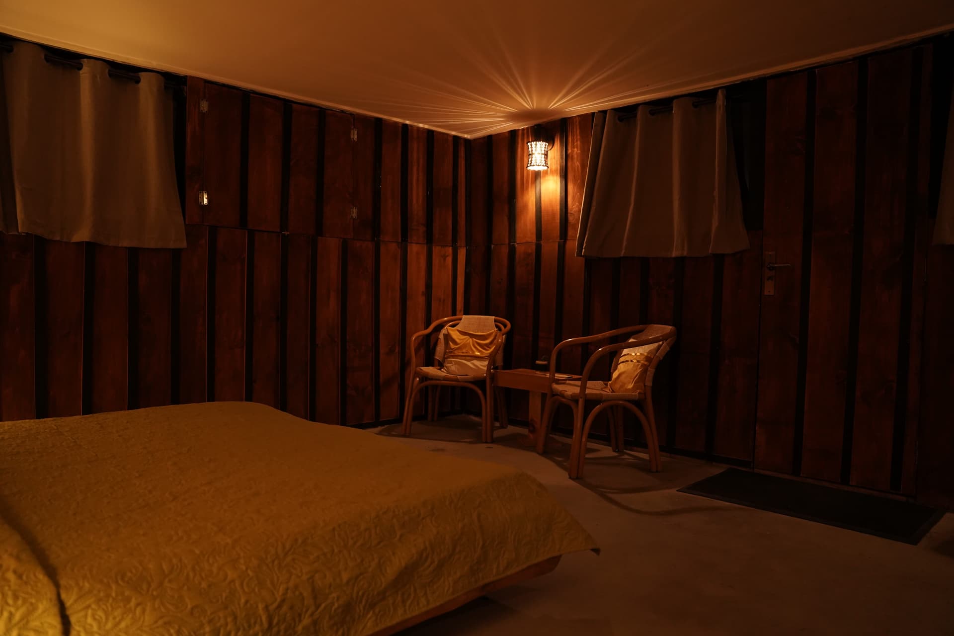 Cozy bedroom corner with golden lighting, curtains, and two wicker chairs