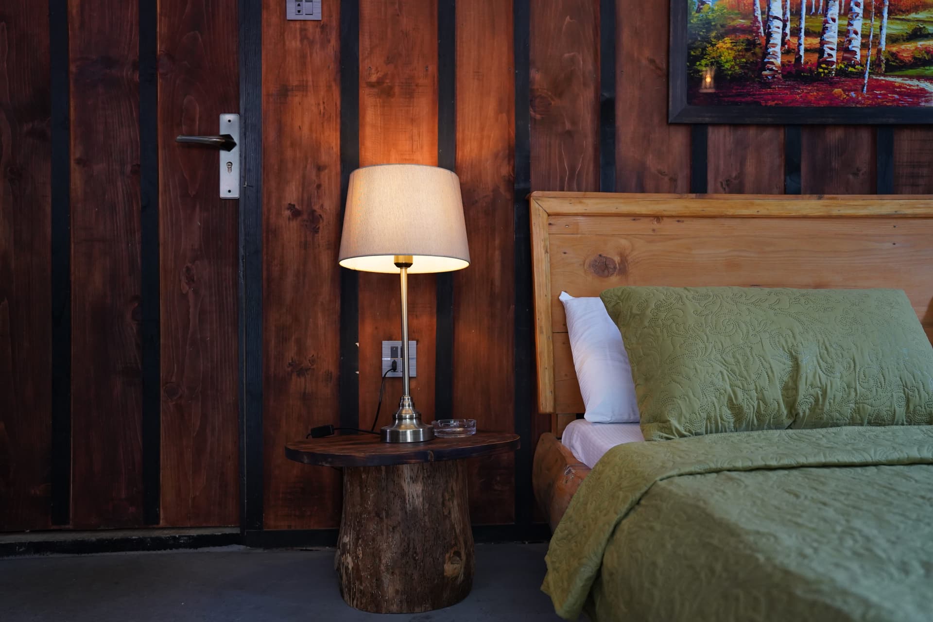 Bedside detail with lamp on rustic stump table, wood headboard, and green bedding