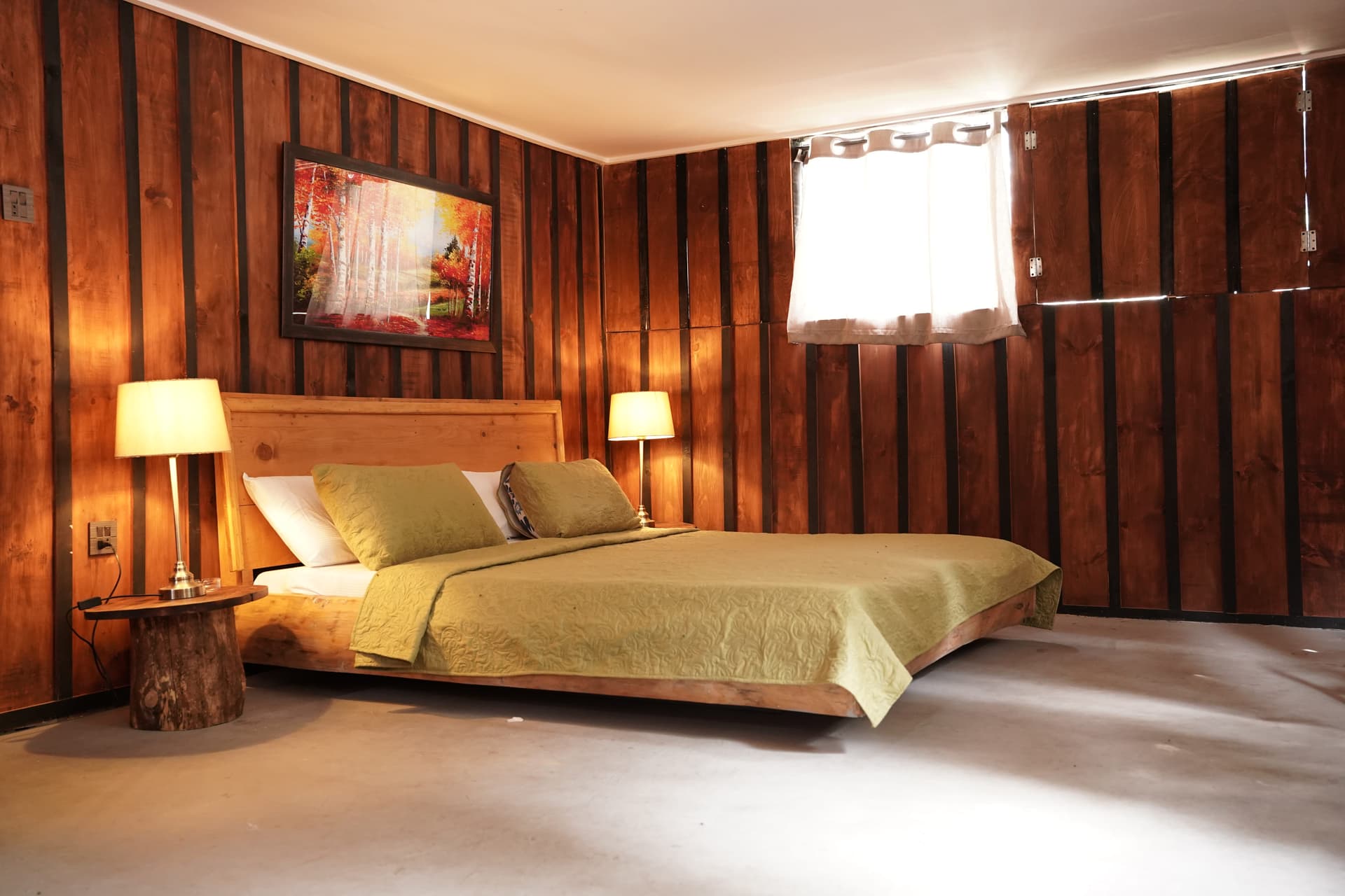 Bright bedroom with wood paneling, olive green bedding, rustic stump side tables, and natural light