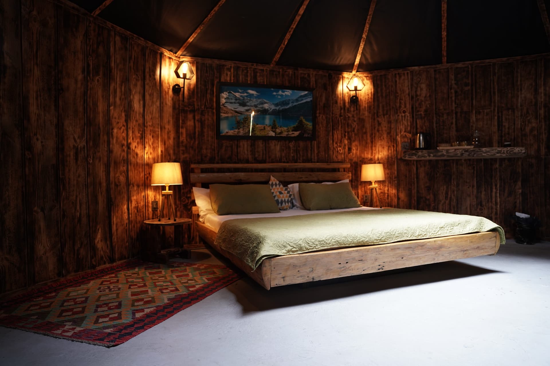 Dramatic bedroom with dark wood walls, wall sconces, geometric wooden ceiling, and sage green bedding